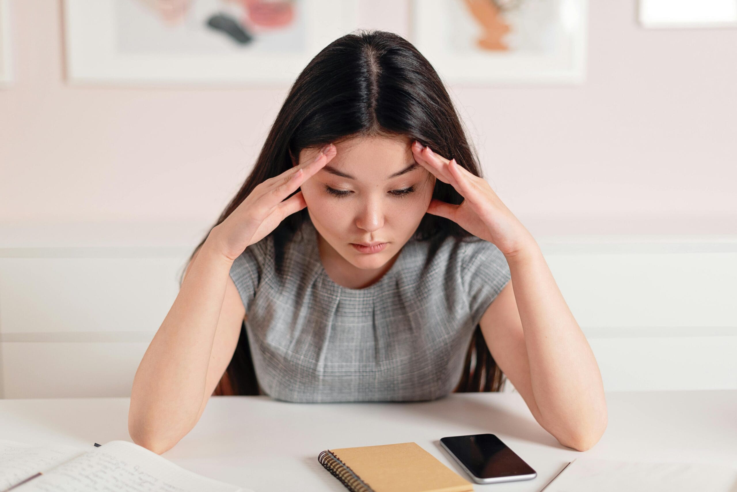teenage girl stressed hands on head looking at notebook and phone experiencing social anxiety and pressure as a teen